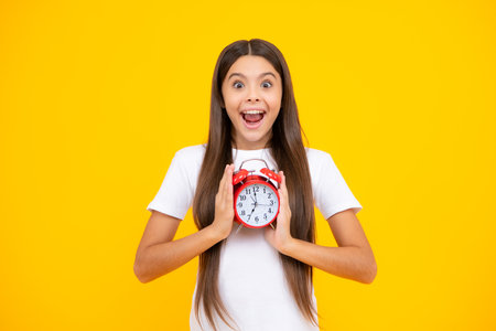 Portrait of teenage girl with clock alrm, time and deadline. Studio shot isolated on yellow...