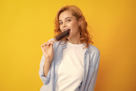 Portrait of beautiful woman eating ice cream on orange yellow background. Girl eating ice pop. Happy excited expression female portrait.の写真素材