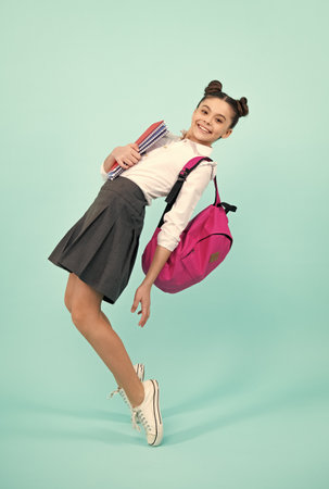 Back to school. Teenager schoolgirl hold book and copybook ready to learn. School children on isolated blue studio background. Happy teenager, positive and smiling emotions of teen girl.の写真素材