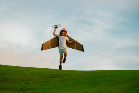 Child pilot aviator with with paper wings or toy airplane dreams of traveling in summer in nature.