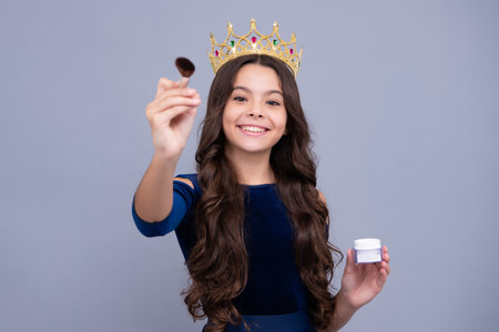 Beauty, make up and kids cosmetics. Teenage girl with brush applying blush to face isolated on grey studio background. Happy face, positive and smiling emotions of teenager girl.の写真素材