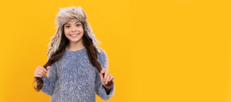 happy kid long hair in hat on yellow background, winter. Banner of child girl in winter hat, studio...