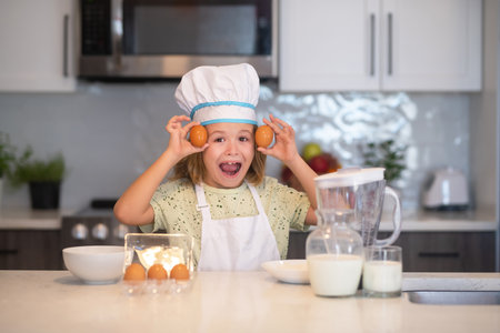 Child chef cook with eggs. Kid chef cook in chef hat preparing food on kitchen. Child making tasty delicious. Cooking meal.の写真素材