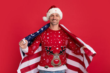 Santa hold american flag. Xmas in united states, usa. Portrait of christmas santa man on red studio background.の写真素材