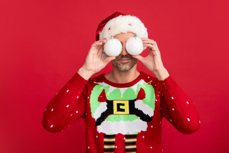 Man in Christmas sweater and Santa hat on red background. Santa with christmas ball.の写真素材