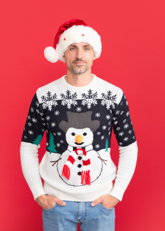 Handsome man in a winter sweater and Santa hat on studio red background.の写真素材