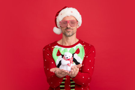 Santa hold christmas toy. Man in Christmas sweater and Santa hat on red background.