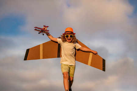 Little child boy is playing and dreaming of flying over the clouds. Little child boy is playing and dreaming of flying. Childhood concept. Little cute boy playing with a toy plane wings.の写真素材
