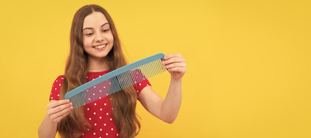 happy kid brushing long hair with comb on yellow background, haircare. Kid girl hair care,...