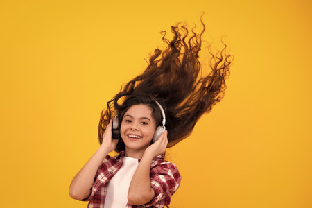 Teenager in modern wireless headphones enjoying song music in audio app, listening to her favorite music over yellow studio background. Happy teenager girl casual wear.の写真素材