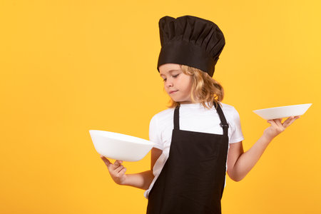 Little cook with cooking plate. Kid in cooker uniform and chef hat preparing food on studio color background. Cooking, culinary and kids food concept.の写真素材