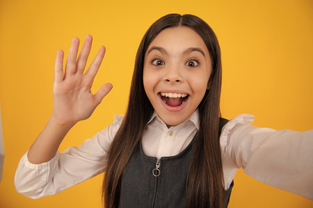 Teenager lifestyle. Beautiful ateenager child girl in moder suit making selfie posingisolated on yellow background.の写真素材