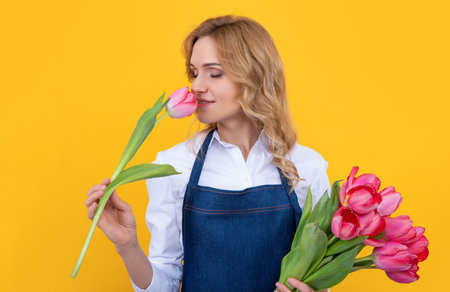 young woman smile in apron with spring tulip flowers on yellow backgroundの写真素材