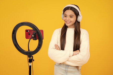 Music kids blog. Teenager child blogger with phone recording video on isolated yellow studio background. Influencer teen girl speaking in front of smartphone.の写真素材