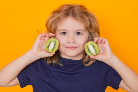 Child hold kiwi in studio. Kiwi fruit. Studio portrait of cute kid boy with kiwi isolated on yellow.の写真素材