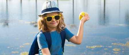 Cute blond kid with binoculars wearing explorer hat and backpack on nature. Child explorer hiking and adventure.の写真素材