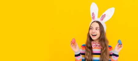 happy teen child in bunny ears and bow tie hold easter eggs on yellow background. Easter child...