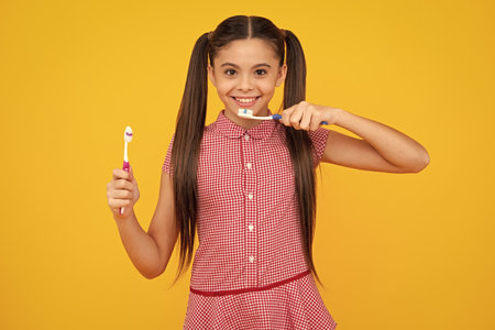 Teenager girl brushing her teeth over isolated yellow background. Daily hygiene teen child hold toothbrush, morning routine. Dental health oral care. Happy teenager, positive and smiling.の写真素材