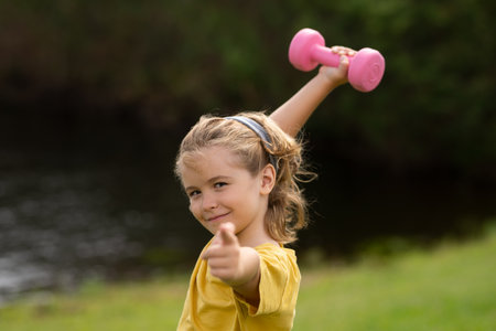 Sport activities at leisure with children. Blonde boy holding dumbbells. Sports exercises for children. Funny child lifting the dumbbells.の写真素材