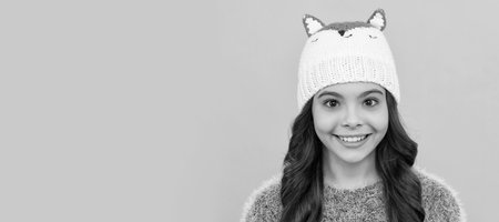 happy child in sweater and hat on yellow background, winter. Child face, horizontal poster, teenager girl isolated portrait, banner with copy space.の写真素材