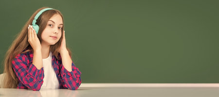 smiling kid with earphones at blackboard, audio accessory. Banner of schoolgirl student. School...