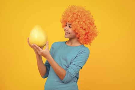 Summer fruits. Teenager child girl hold citrus fruit pummelo or pomelo, isolated on yellow background. Kid healthy eating. Happy teenager portrait. Smiling girl.の写真素材