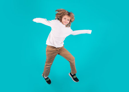 Funny boy jumping in air. Energetic kid boy jumping and raising hands up. Full length body size...