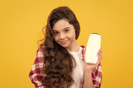 Teenager child girl with bottle shampoo conditioners or shower gel. Kids hair care. Hair cosmetic product, shampoo bottle. Happy teenager, positive and smiling emotions of teen girl.の写真素材
