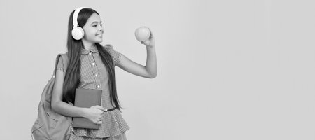 knowledge day. concept of education. kid in headphones with book and apple for lunch. Horizontal isolated poster of school girl student. Banner header portrait of schoolgirl copy space.の写真素材