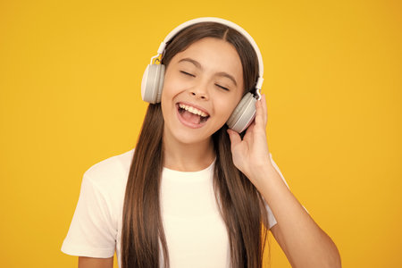 Child music concept. Teenager child girl dances in rhythm of melody, listens song in headphones. Child listening to music through earphones.の写真素材