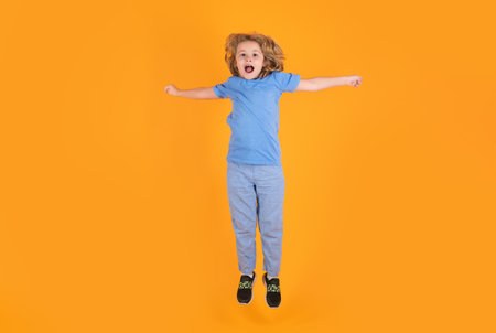 Full length of excited kid jumping. Energetic kid boy jumping and raising hands up on isolated...