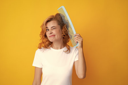 Surprised amazed girl combing hair. Redhead woman with a comb, isolated on yellow background. Woman...