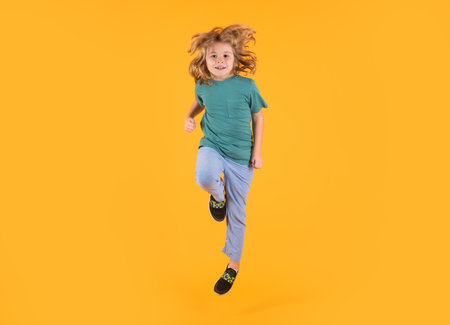 Energetic kid boy jumping and raising hands up on isolated studio background. Full length body size...