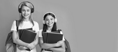 Mother and daughter child banner, copy space, isolated background. mother and daughter in earphones hold notebook and backpack ready to study, ebook.の写真素材