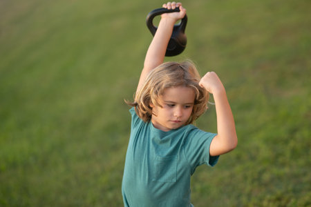Child lifting the kettlebell in park outside. Cute child boy pumping up arm muscles with kettlebell. Fitness kids with dumbbells.の写真素材