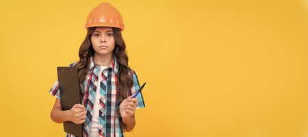 Builder teenager girl in helmet. serious kid in construction helmet hold in clipboard and pen. Child builder in helmet horizontal poster design. Banner header, copy space.の写真素材