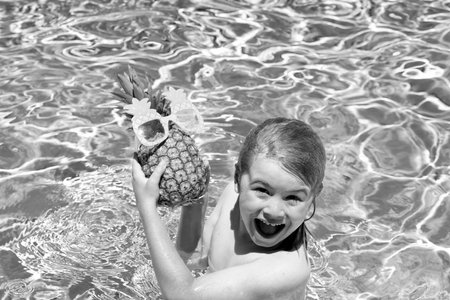 Happy kid in swimming pool on summer day. Child play in tropical resort. Summer vacation. Summer funny pineapple fruit for children.の写真素材