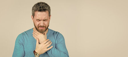 mature man with beard suffer from sore throat on grey background, cold. Man face portrait, banner...