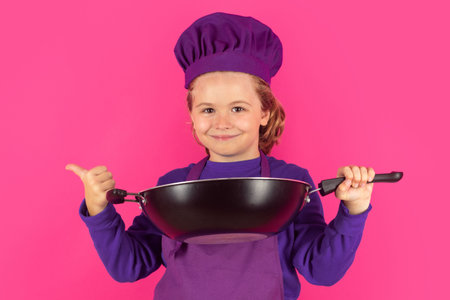 Kid cook with cooking pan. Child chef cook, studio portrait. Kids cooking. Teen boy with apron and chef hat.の写真素材