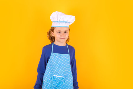 Kid in cooker uniform and chef hat preparing food on studio color background. Cooking, culinary and kids food concept.の写真素材