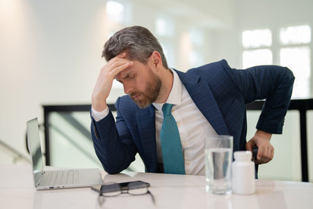 Sad man with laptop got migraine touches her head because of pain. Man manager with strong headache. Overworked freelancer or manager at office.の写真素材