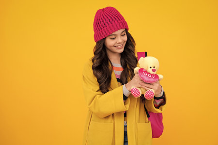 Back to school. Teenager schoolgirl in autumn wear hold toy. School children with favorite toys on isolated yellow studio background. Happy teenager, positive and smiling emotions of teen girl.の写真素材