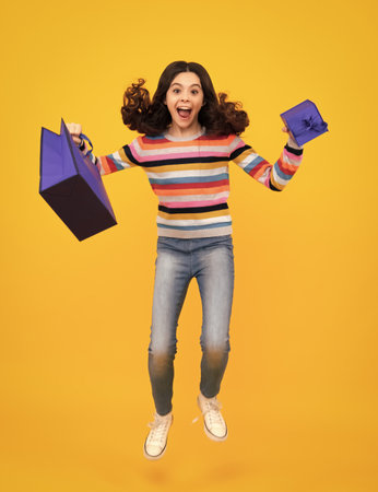 Sale and shopping concept. Teen girl holding shopping bags, isolated on studio background. Amazed teenager. Run and jump. Excited teen girl.の写真素材