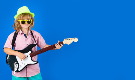 Caucasian little boy learning to play guitar. Funny little hipster musician child playing guitar.の写真素材
