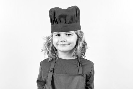 Funny kid chef cook studio portrait. Cooking children. Chef kid boy in form of cook. Child boy with apron and chef hat preparing a healthy meal in the kitchen. Cooking process.の写真素材