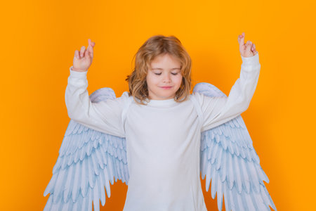 Child angel crossed fingers with lucky and hope, good luck. Beautiful little angel. Isolated studio shot. Cute Pretty child with angel wings. Cupid, valentines day concept.の写真素材