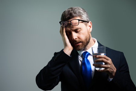 Tired man having a terrible headache. Exhausted man feeling unhealthy, upset about headache illness. Stressed middle-aged man with headache isolated on gray. Migraine and headache concept.の写真素材