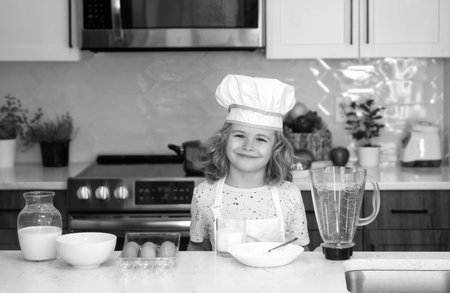 Funny little kid chef cook wearing uniform cook cap and apron cooked food in the kitchen. Kids are preparing the dough, bake cookies in the kitchen.の写真素材