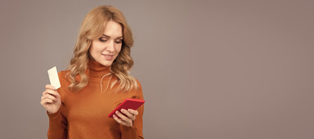 Girl pay with bank card on smart phone grey background copy space, mobile banking. Woman portrait, isolated header banner with copy space.の写真素材