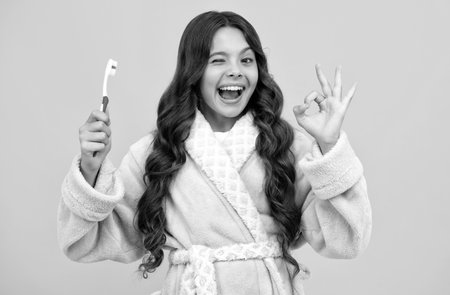 Morning brushing teeth. Portrait beautiful teen holding toothbrush brushing teeth isolated on yellow background, Dental health concept. Amazed teen girl. Excited expression, cheerful and glad.の写真素材